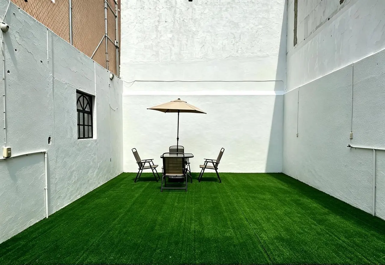Terraza de la clínica con piso de pasto sintético, muros blancos y una reja al fondo